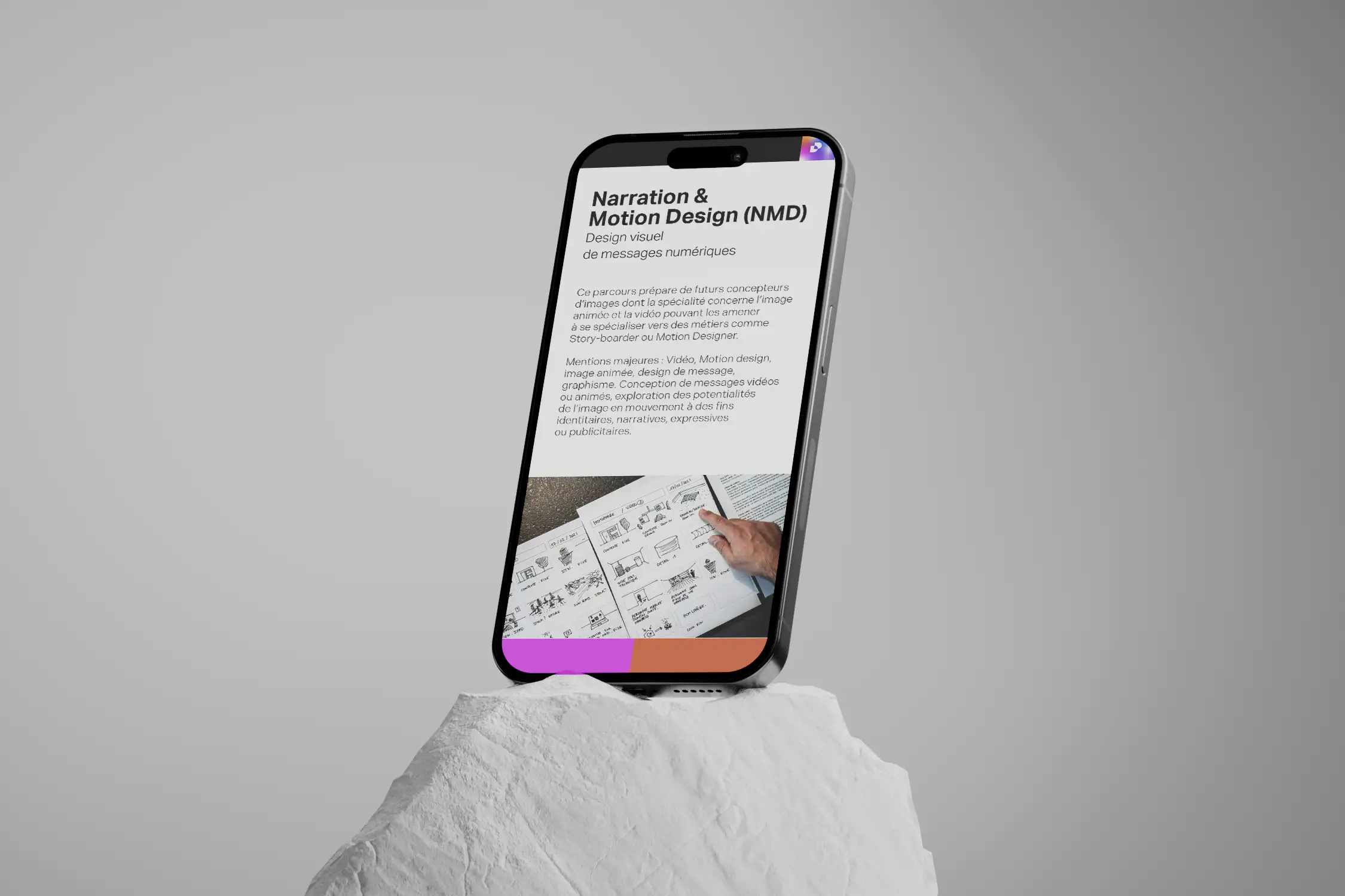 iPhone posé sur une pierre blanche affichant la page 'Narration et Motion Design' du site du Lycée Jean Monnet, contenant des éléments textuels, une photo de story-board et des encarts rose et orange.